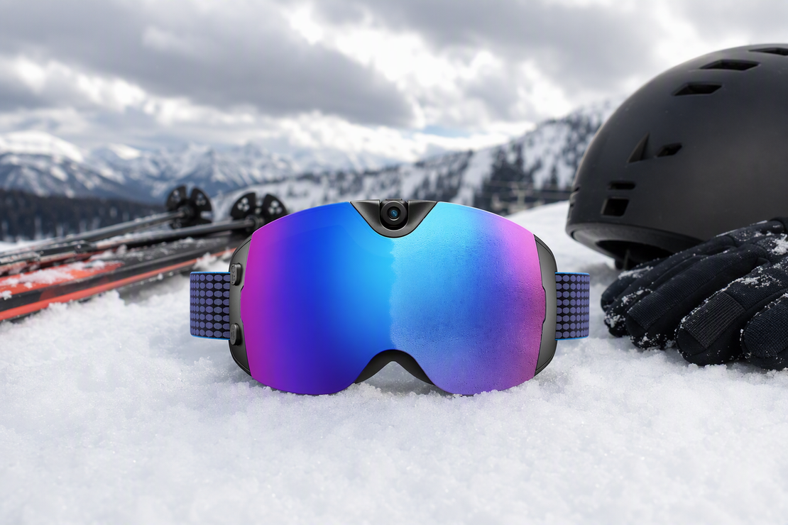 Camera-equipped snow goggles resting on packed snow beside ski gear under mixed mountain light