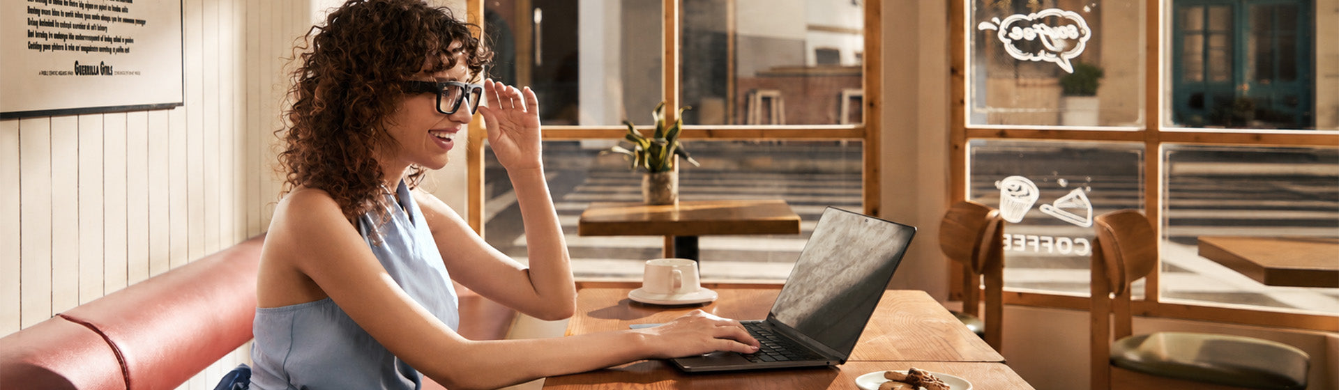 Woman on a couch using a laptop and touching the temple of OhO Sunshine Edge camera glasses