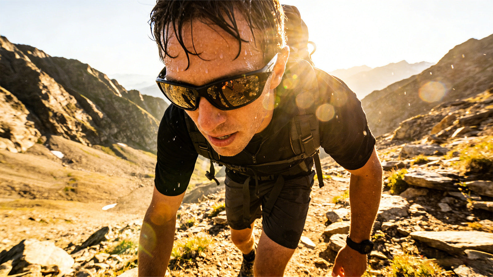 Man wearing sport sunglasses while climbing a rocky mountain trail in bright sunlight