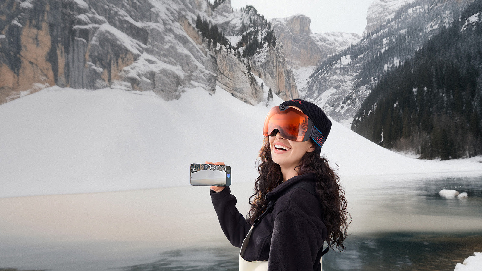 Smiling woman holding smart ski goggles with camera in front of snowy mountains