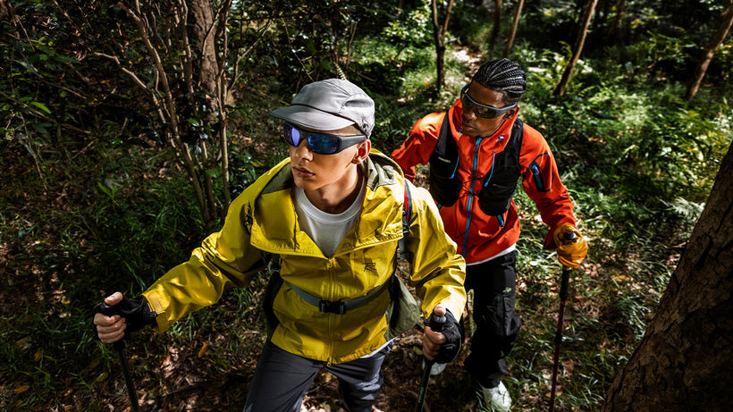 Two hikers wearing smart camera glasses trekking through a lush forest trail