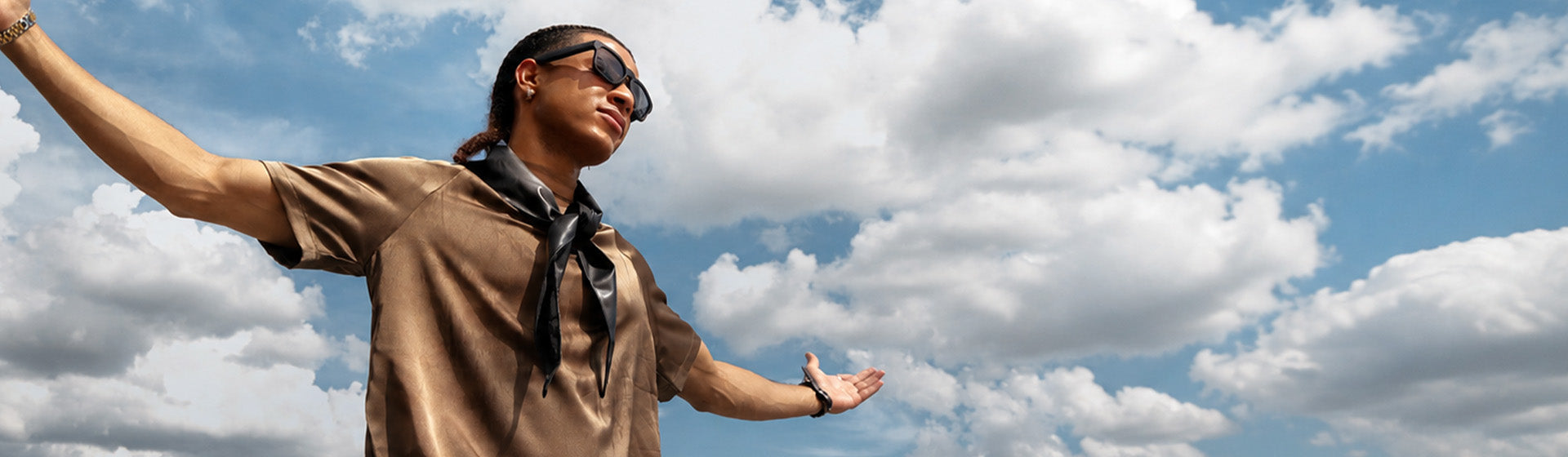 Person in a tan shirt against a bright sky wearing OhO Sunshine Bluetooth audio sunglasses