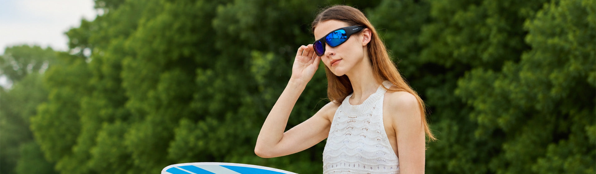 Woman by the water adjusting OhO Sunshine Vidsoul camera sunglasses with blue mirrored lenses
