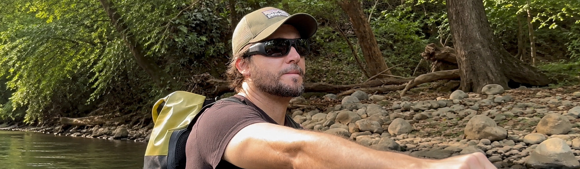 Man on a river bank in a cap wearing OhO Sunshine Brave 4K camera sunglasses