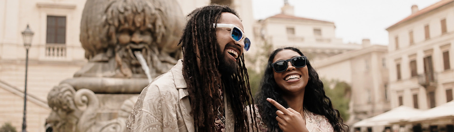 Two friends beside a stone monument wearing OhO Sunshine Elite Bluetooth sunglasses