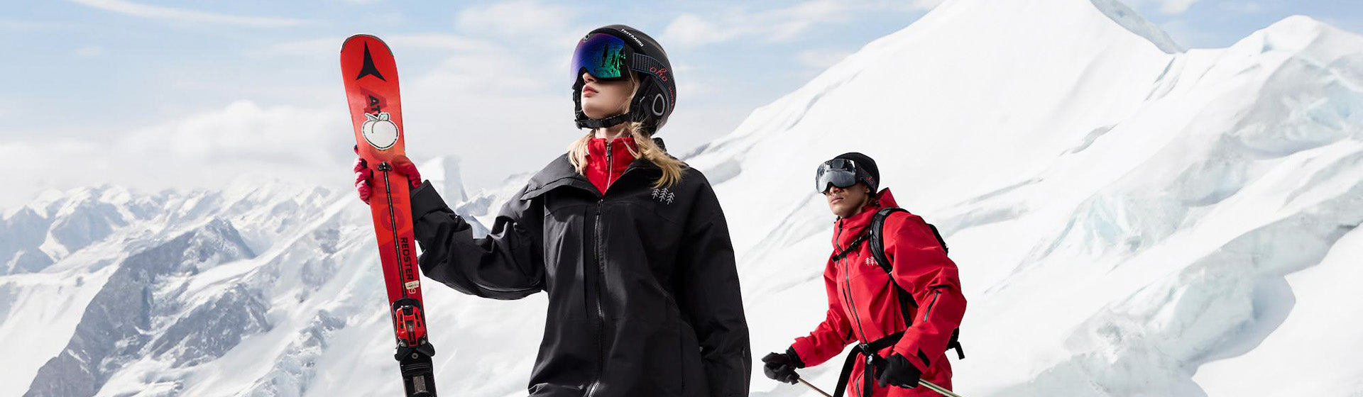 Two skiers holding red skis on a snowy slope wearing OhO Sunshine Skyshot 4K camera goggles